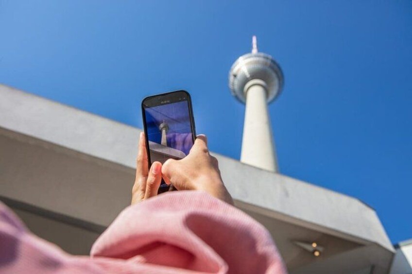 A person holding a smartphone, taking a photo of a tower against a clear blue sky. 4