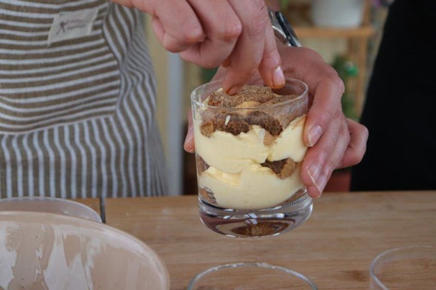 A person assembling a layered dessert in a clear glass. 4