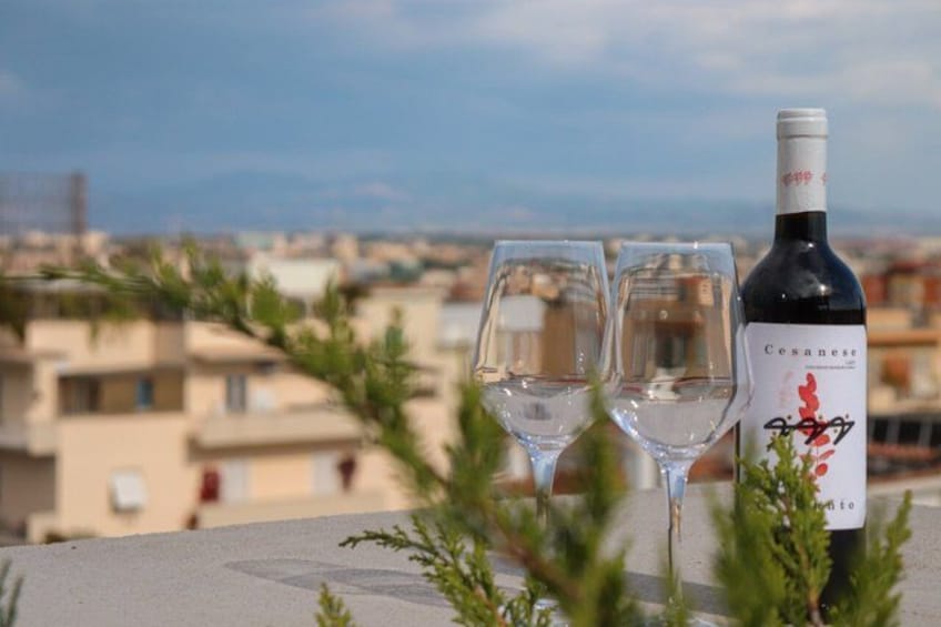 A bottle of wine and two glasses on a rooftop with a cityscape in the background. 2
