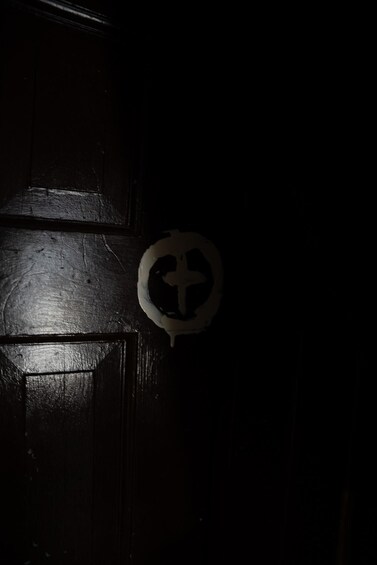 Una puerta de madera oscura con un objeto circular blanco que presenta una cruz. 3
