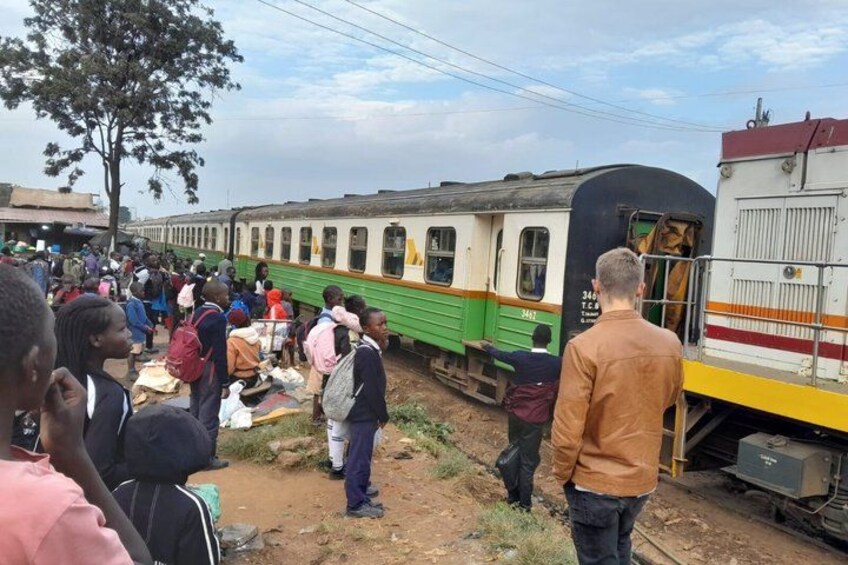 A train with passengers boarding and alighting, a crowd of people, and a tree in the background. 5