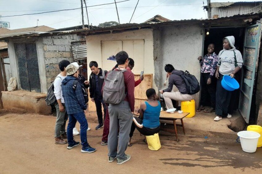 A group of people gathered around a table outside a building with a corrugated metal roof. 2