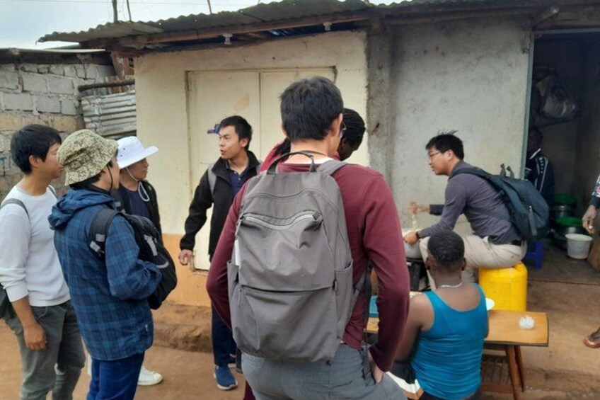 A group of people gathered around a table in a rustic setting with a small building in the background. 4