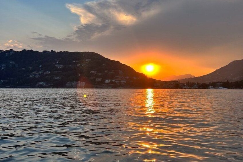A sunset over a lake with reflections on the water, surrounded by hills and buildings. 4