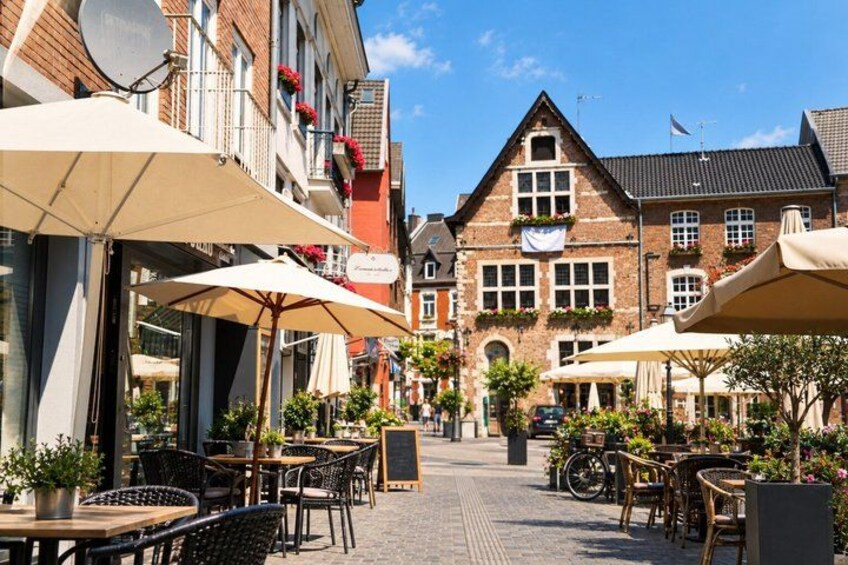 A cobblestone street lined with outdoor cafes, brick buildings, and potted plants. 2