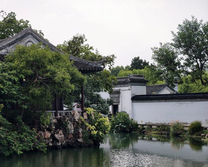 A traditional Chinese garden with a pond, white walls, and green trees. 5