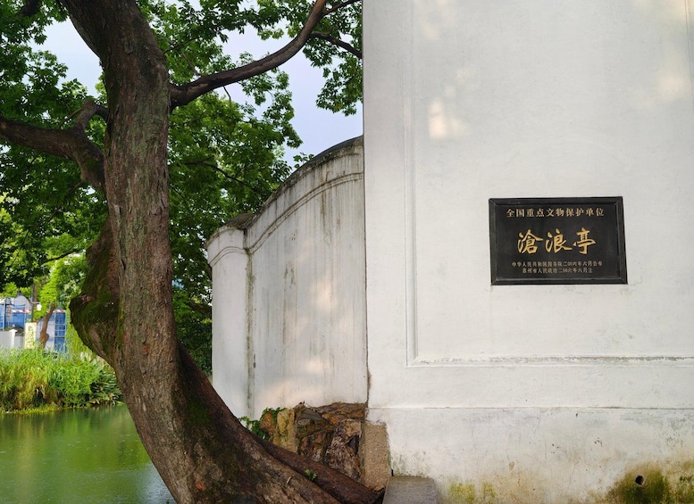 A white wall with a plaque, a tree, and a body of water. 3