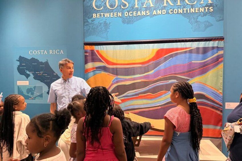 A group of people at a Costa Rica exhibit with a map and a colorful oceanic background. 4