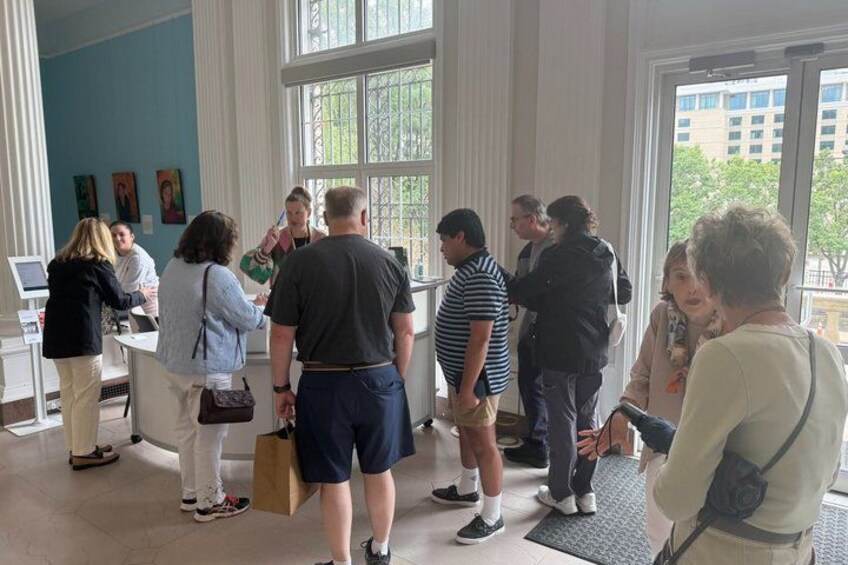 A group of people in a room with large windows, standing and conversing. 5
