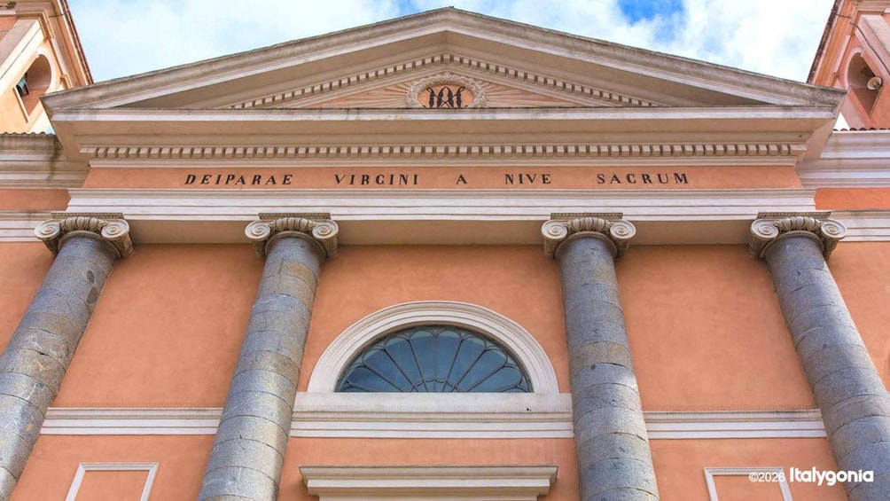 A neoclassical building facade with inscriptions 'DEIPARAE VIRGINI A NIVE SACRUM' and a central arched window. 3