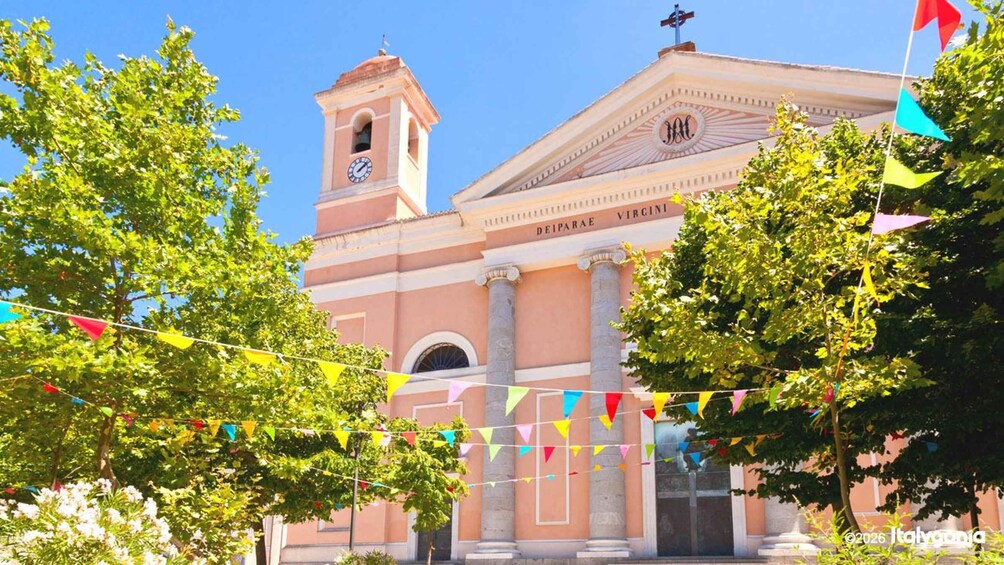 A building with a clock tower and columns, surrounded by trees and colorful flags. 1
