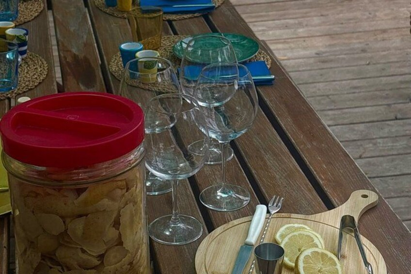 A wooden table with a jar of food, empty wine glasses, a plate with lemon slices, and a knife. 5