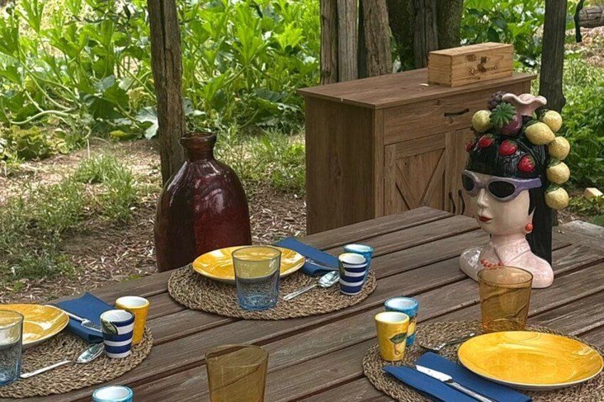 A wooden picnic table set outdoors with yellow plates, blue and yellow cups, and a decorative headpiece. 4