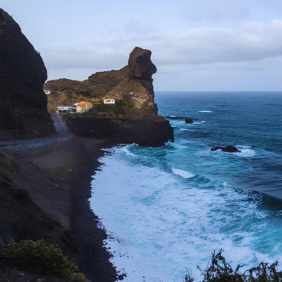 A coastal landscape with a prominent rock formation, a road leading to a building, and the ocean. 2