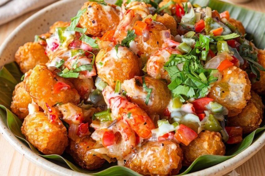 A bowl of tater tots topped with shrimp, diced tomatoes, and a green herb garnish. 4
