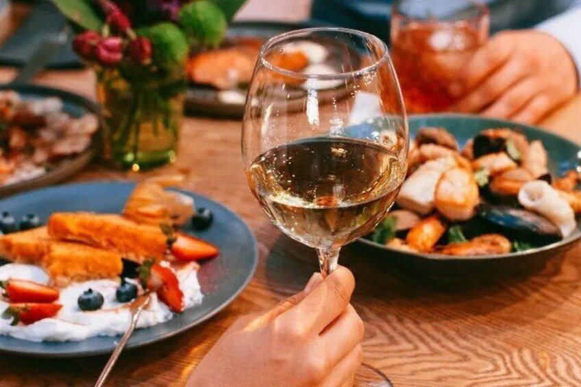 A person holding a wine glass, a plate with seafood, and a bowl of food on a wooden table. 3