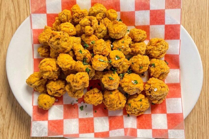 A plate of golden-brown fried food items, possibly fritters, garnished with herbs, on a checkered paper. 5