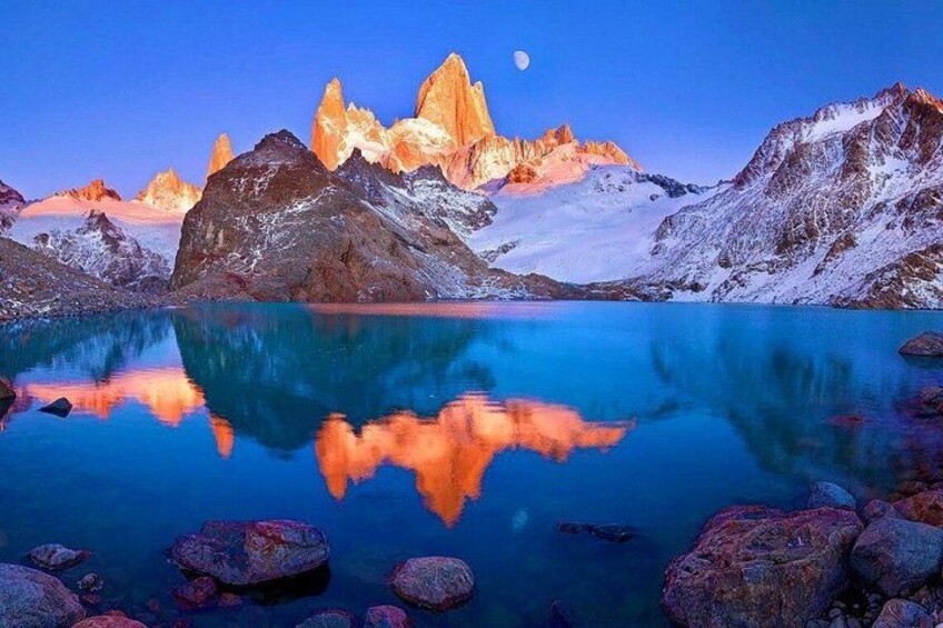 A mountain range with a reflective lake, a clear sky, and a visible moon. 1