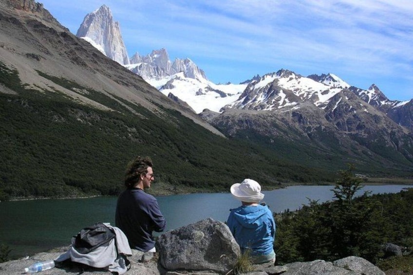 Two people sitting by a lake with mountains in the background. 3