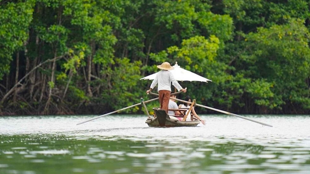 A person in a boat with a large umbrella, surrounded by water and greenery. 1