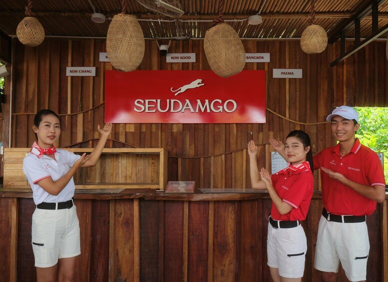 A wooden structure with a red banner reading 'SEUDAMGO' and hanging signs indicating locations like 'KOH CHANG,' 'KOH KOOD,' 'BANGKOK,' and 'PATAYA.' 4