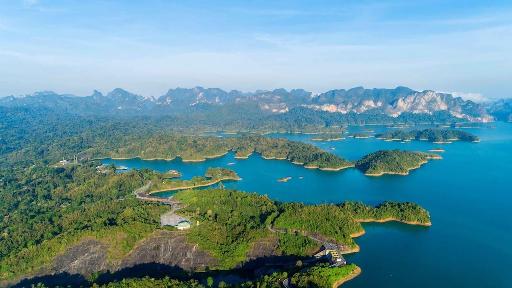 A coastal landscape with numerous islands surrounded by clear blue waters, dense green forests, and mountainous terrain in the background. 5
