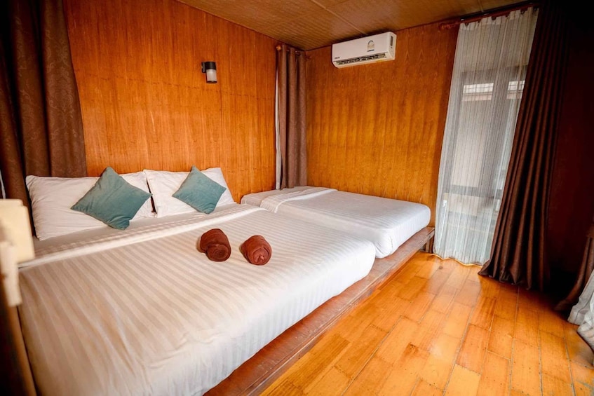 A wooden-paneled room with two beds, a wall-mounted air conditioner, and a window with curtains. 4