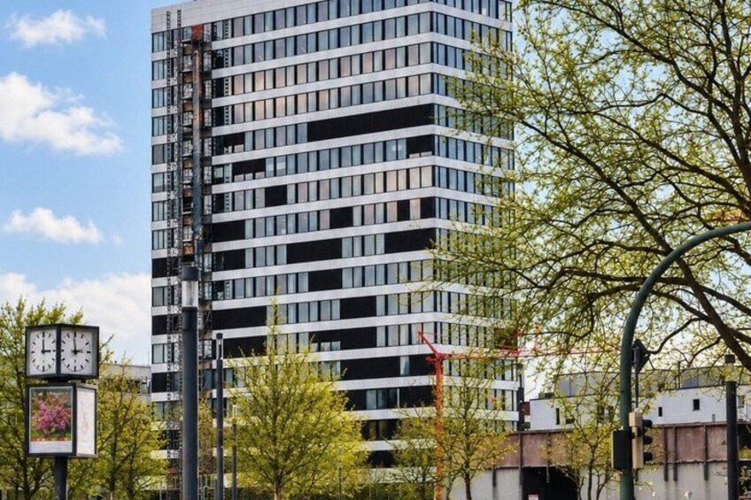 A tall building with a clock, surrounded by trees and a traffic light. 3