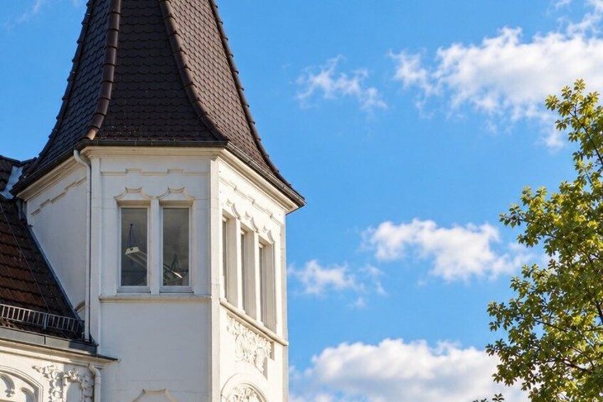 A building with a white facade, a dark roof, and a clear blue sky with clouds. 2