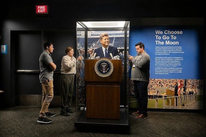 A historical exhibit with a podium, a person in a suit, and a crowd in the background. 1