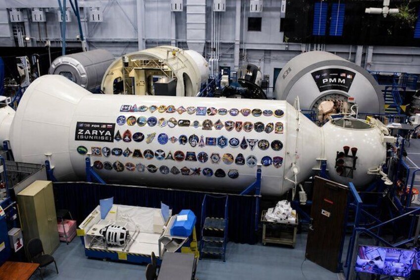 A large cylindrical structure with multiple panels, labeled 'ZARYA SUNRISE,' surrounded by various equipment and machinery. 5