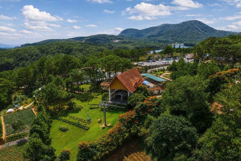 A lush green landscape with a prominent house surrounded by dense vegetation, a clear sky, and distant mountains. 5