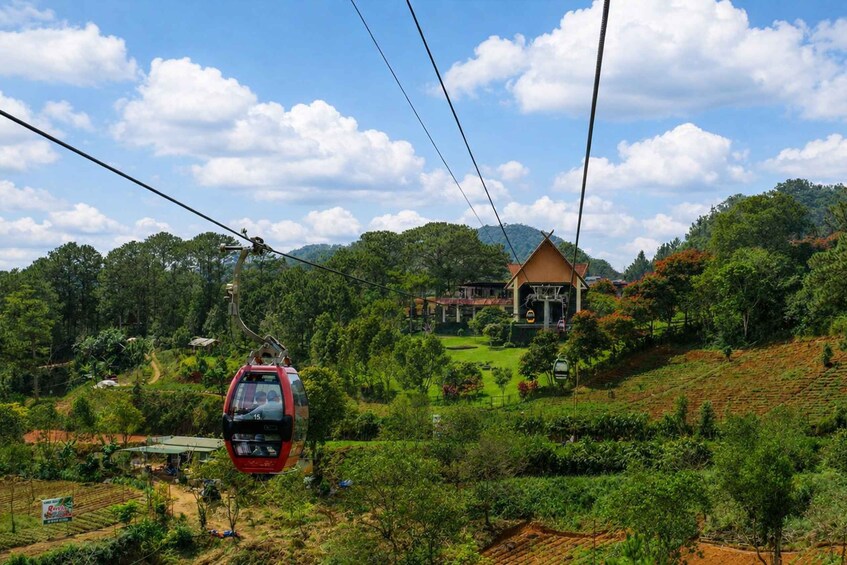 A cable car moving along a cable, a building, and a lush green landscape with trees and a hill in the background. 3
