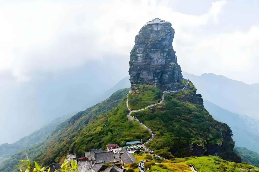 A mountain with a tall, narrow rock formation and a winding path leading to a traditional building at its base. 3