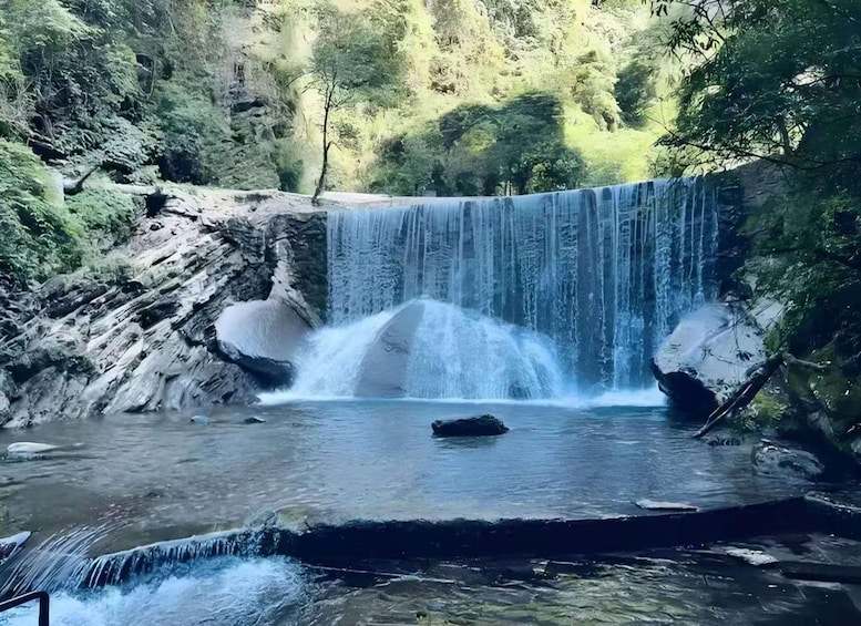 A waterfall cascading into a pool surrounded by rocky terrain and dense greenery. 4