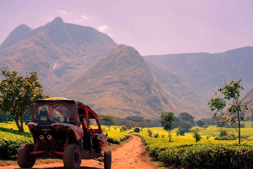 A red off-road vehicle on a dirt path with mountains in the background. 1
