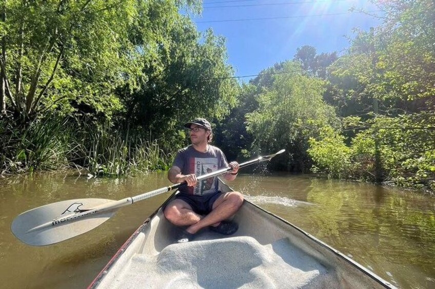 A person paddling a canoe on a river surrounded by dense greenery. 1