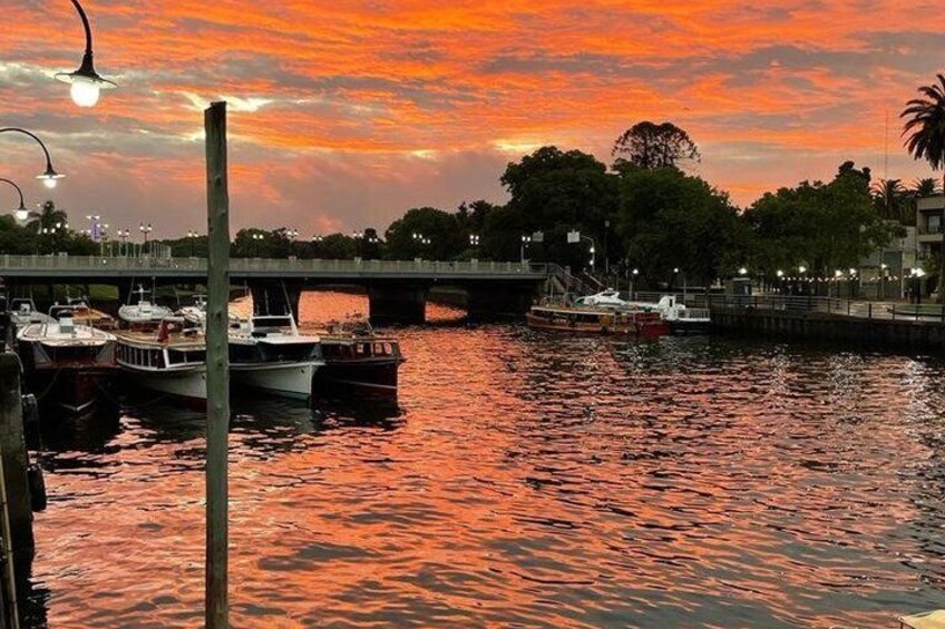 A sunset over a river with boats docked, a bridge, and trees in the background. 5