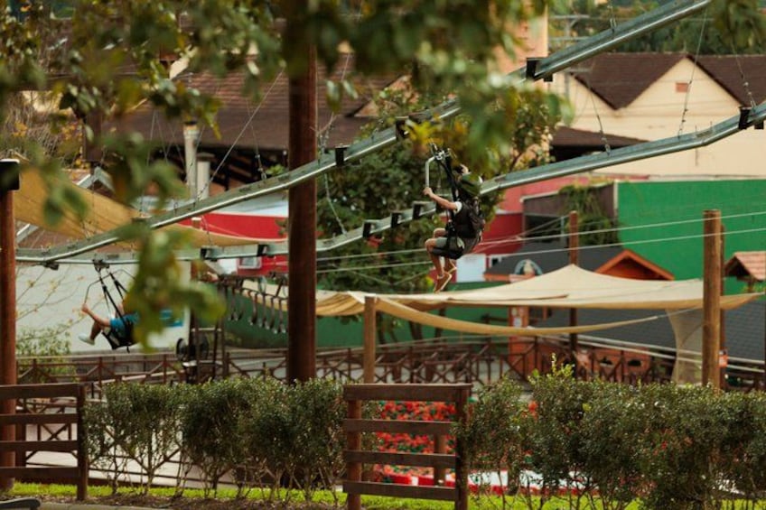 A person swinging on a rope course in an outdoor setting with trees and buildings in the background. 3