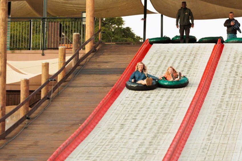 A wooden boardwalk leading to a water slide with two people in tubes. 2