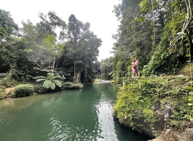 Ein Fluss, umgeben von dichtem Wald, mit einer Person, die auf einer Felsstufe steht. 1