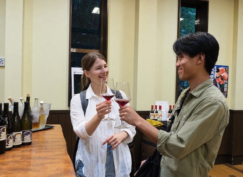 Two people holding wine glasses at a bar with bottles of wine and a poster in the background. 5