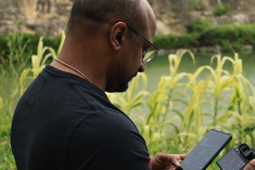 A person holding a tablet outdoors with greenery and a body of water in the background. 3