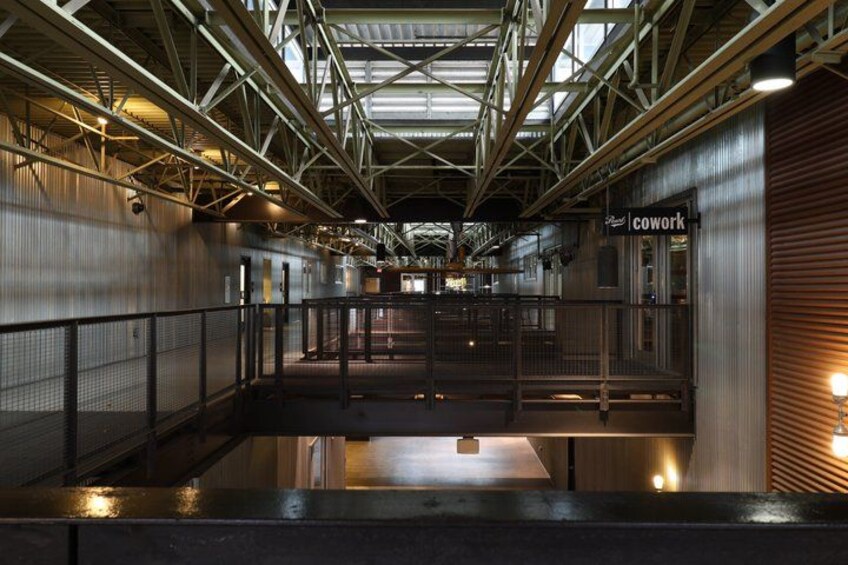 An industrial interior with metal structures, a sign reading 'cowork,' and a mezzanine level. 1