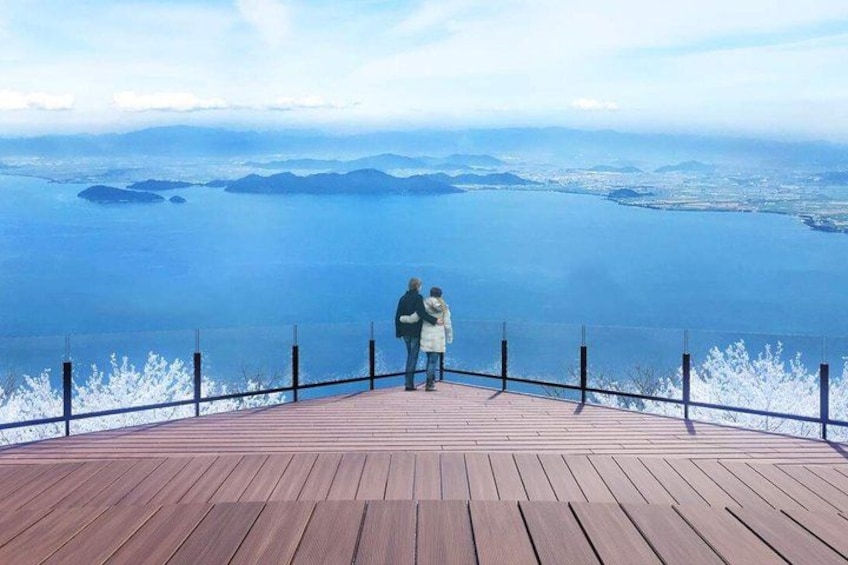 A wooden observation deck with a railing, overlooking a vast body of water and distant land. 4