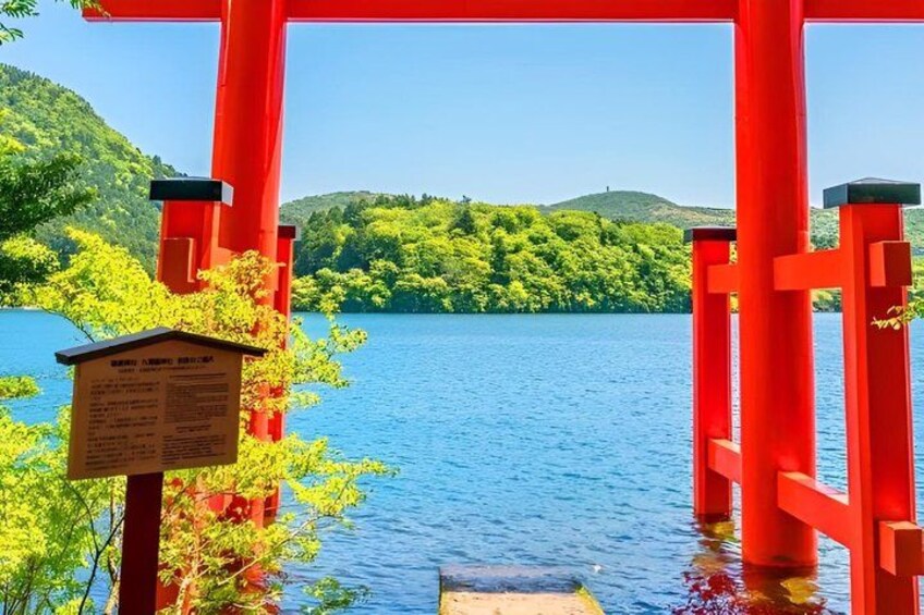 A red torii gate with a sign, a wooden platform, and a lake with green hills in the background. 5