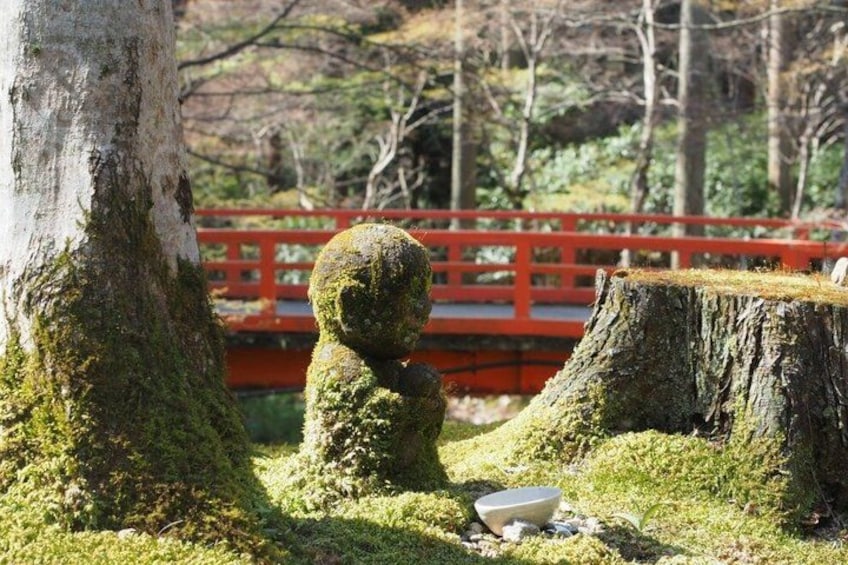 A moss-covered statue, a red bridge, and a tree stump in a park. 3
