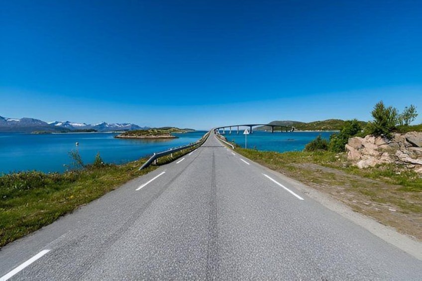 A road leading to a bridge over a body of water with mountains in the background. 3