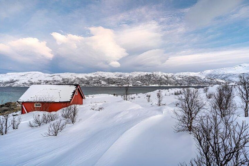 A red wooden house on a snow-covered hill, a lake in the background, and snow-covered trees. 5