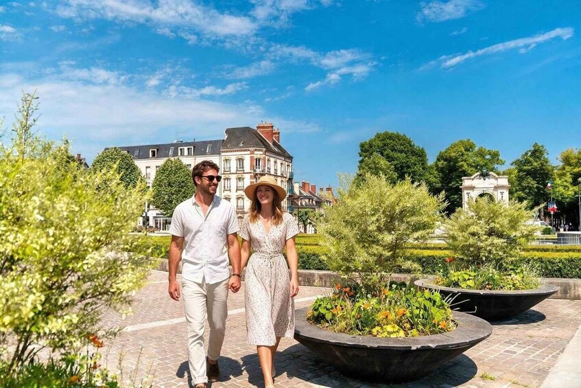 Un couple se promène dans un parc où se trouve une grande fontaine et, en arrière-plan, des bâtiments historiques. 2